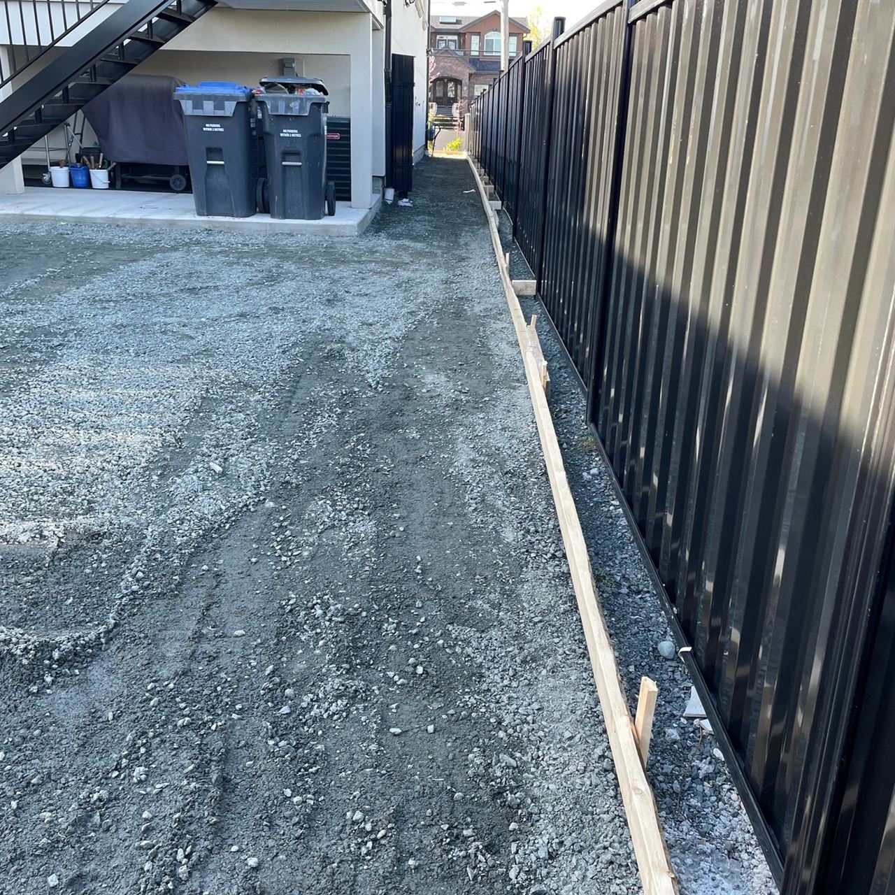 Asphalt paving prep — gravel base graded alongside metal fence line