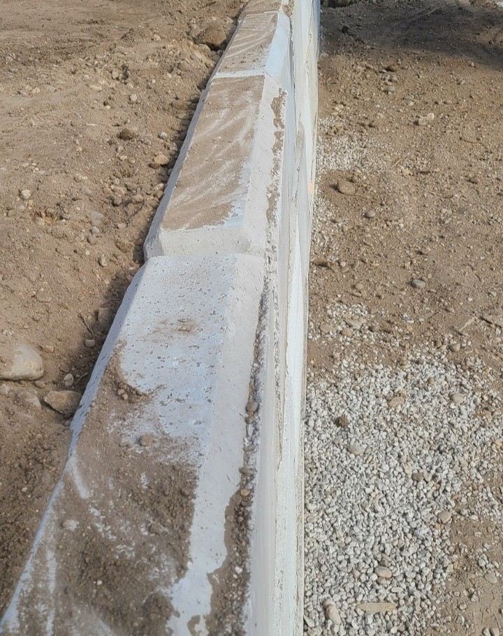 Concrete lock block wall install — freshly poured curb wall in a dirt lot